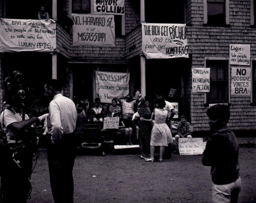 People standing in front of a triple decker home decorated with protest signs.