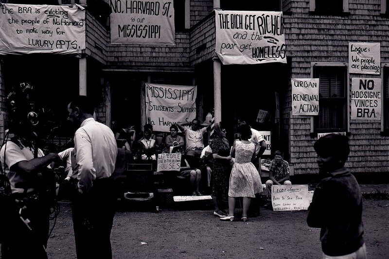 People standing in front of a triple decker home decorated with protest signs.