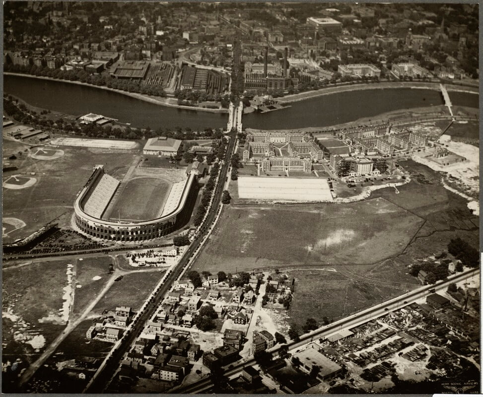 An aerial view of a city cut in half by a river. There is a large area of empty land and a large stadium in the upper left side.
