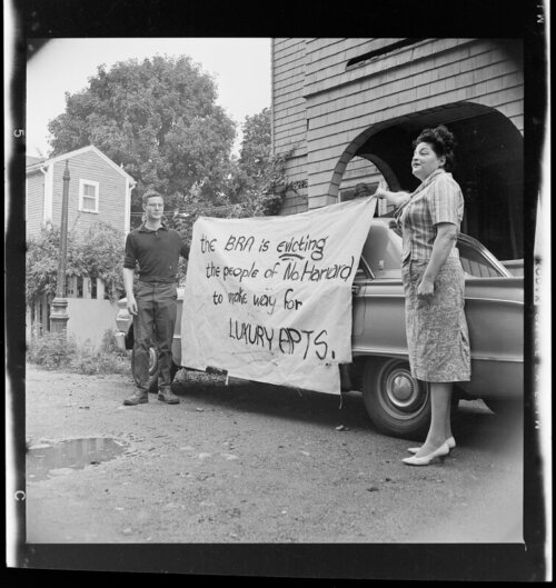 A man and woman holding a sign that says "the BRA is evicting the people of No. Harvard to make way for luxury apts."