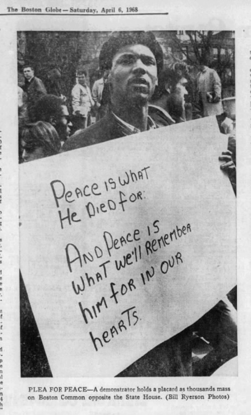 A Black man in a crowd of demonstrators holding a sign that says "Peace is what he died for and peace is what we'll remember him for in our hearts."