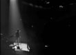 A man stands in a spotlight on a stage in front of a dark stadium.