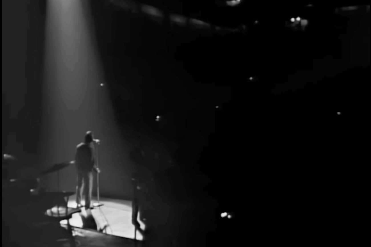 A man stands in a spotlight on a stage in front of a dark stadium.