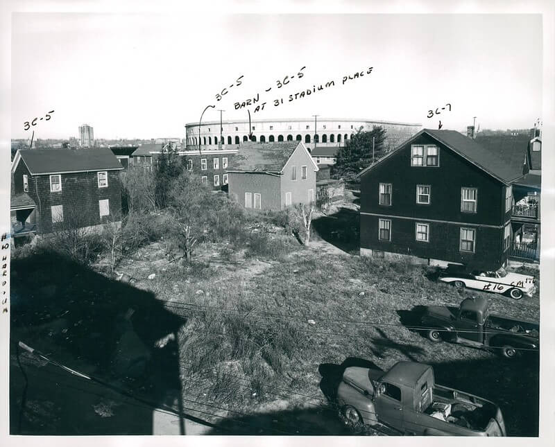 View of a neighborhood of three story homes around a central green space. There is a stadium in the background.
