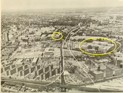 An aerial map of a city neighborhood with white lines cutting through the middle showing the possible route of a highway. Two buildings are circled in yellow.