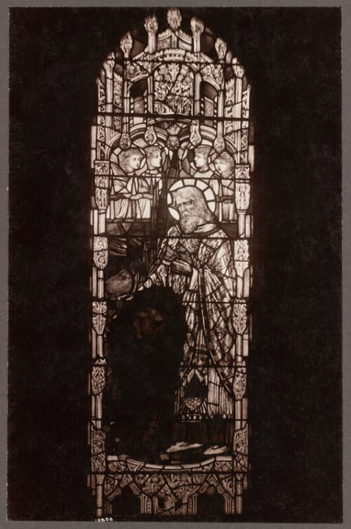 A black and white image of a stained glass window with a bearded saint petting a lion with angels floating behind him.