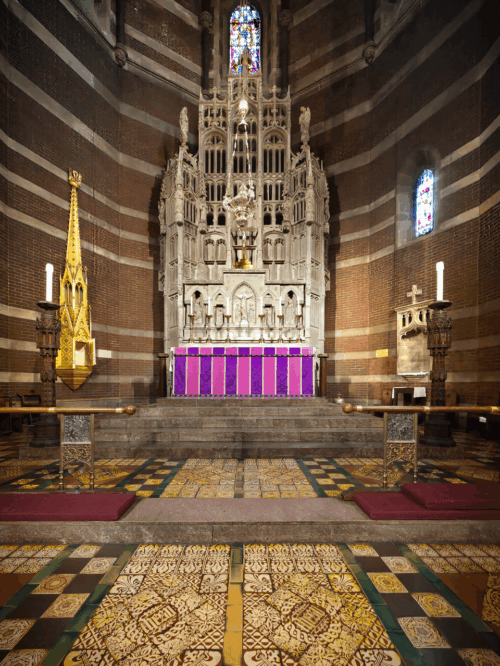 A church altar with tall gothic stone decorations in front of a table with pink and purple cloth.