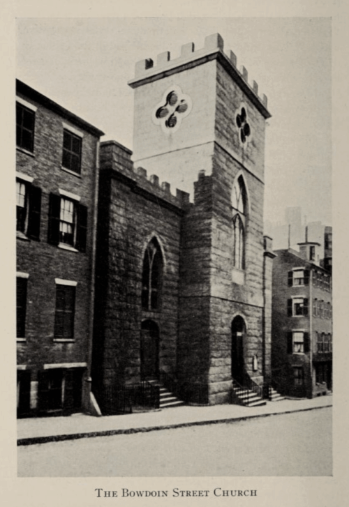 Image of a church between two townhouses with a crenelated tower in the center with clover shaped windows.