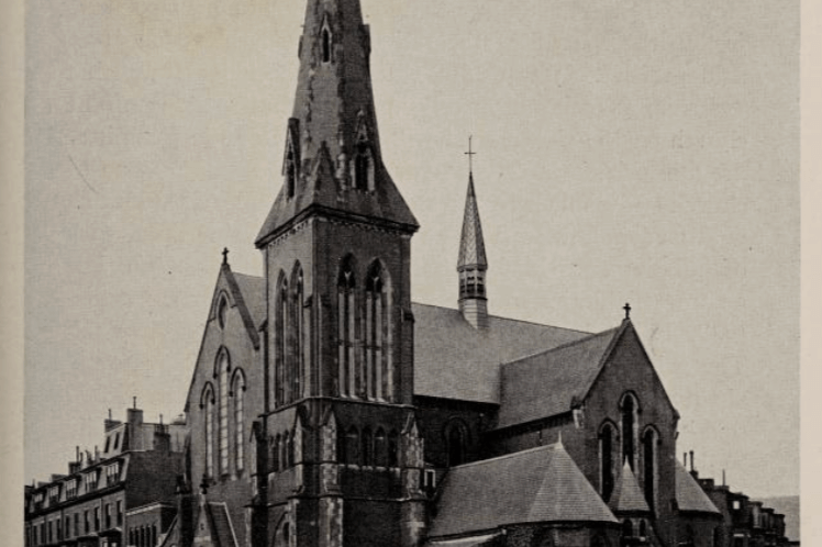 A church building with a tall spire and a chapel coming off the side.