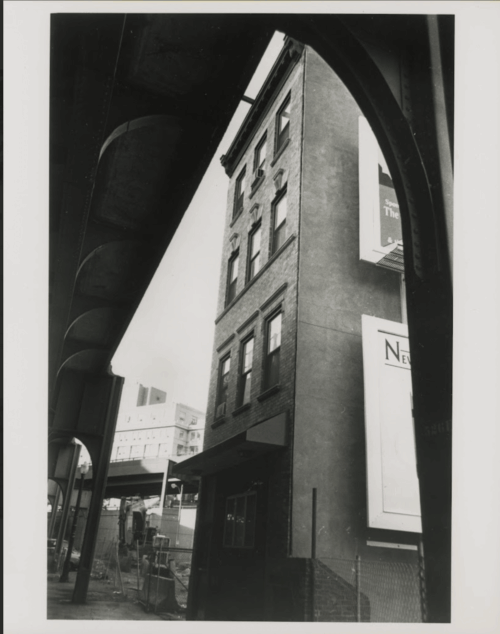 A four story tenement building next to an elevated train track.
