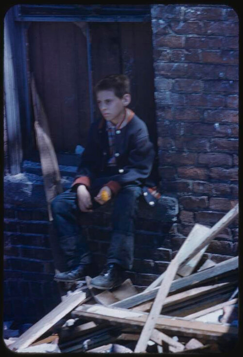 A photo of a boy staring into the distance while he sits on a pile of rubble.