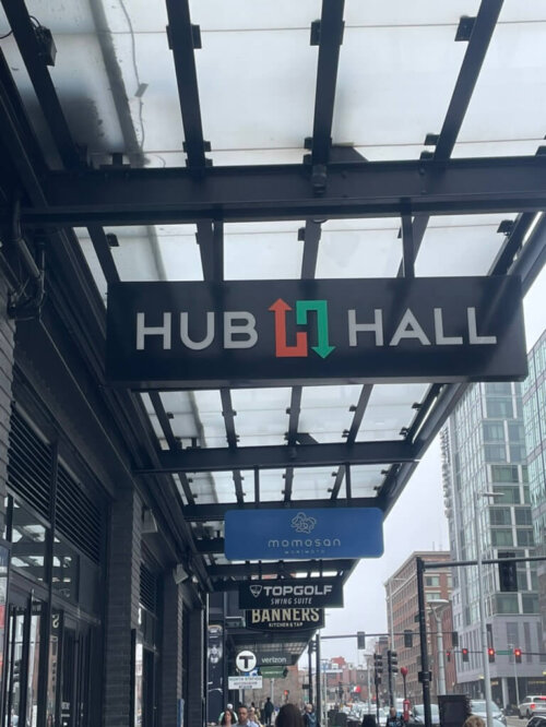 A photo looking up at a sign that says "HUB HALL" under a glass awning.