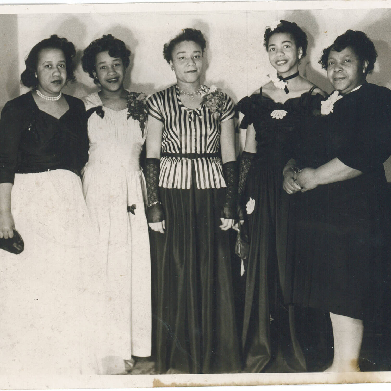 Five women wearing fancy dresses facing the camera.