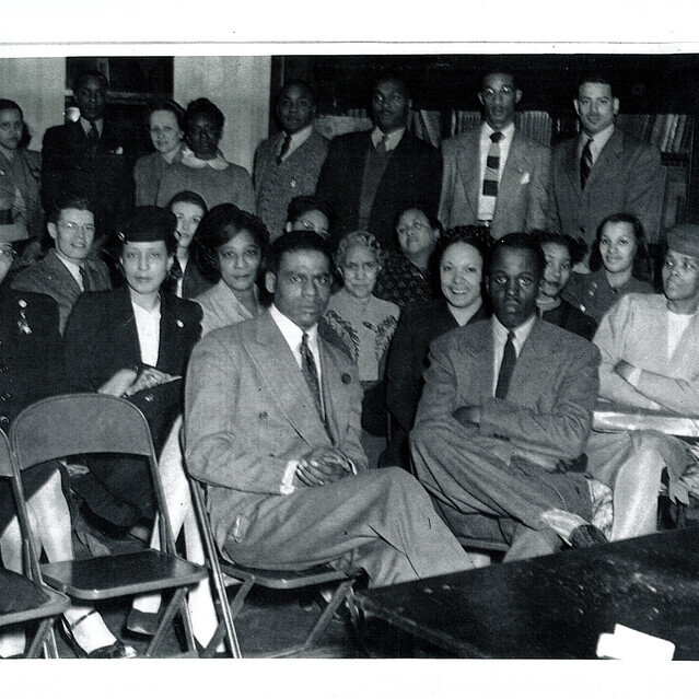 A group of men and women in suits and skirts sitting on folding chairs.