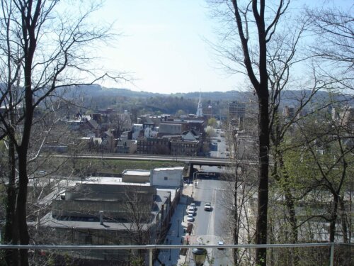A view of a downtown area with a road running up and down and a rail road crossing running left to right. There are mountains in the distance and a church steeple.