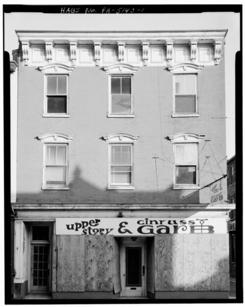 A three story building with a boarded up shop on the ground floor.