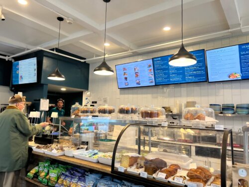 The interior counter of a cafe with baked goods in vitrines and digital menu displays.