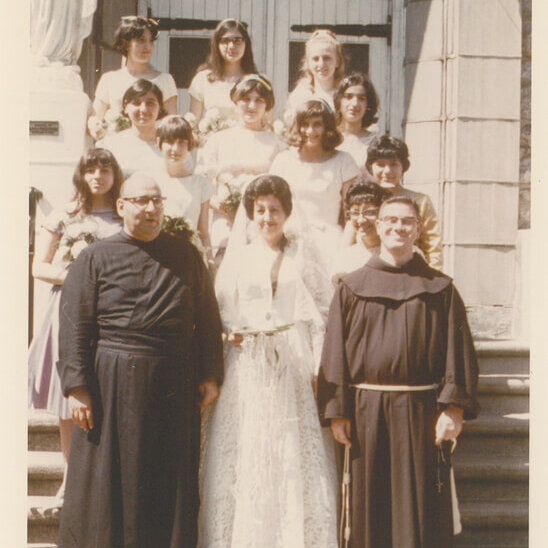 A group of women in white standing on stairs. There are also two priests in traditional monk clothes.