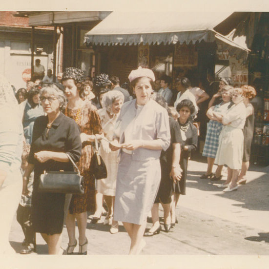 A group of women and children in their Sunday best on a street.