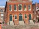 A three story brick building in a federal style with large arched windows and doors facing a paved courtyard.