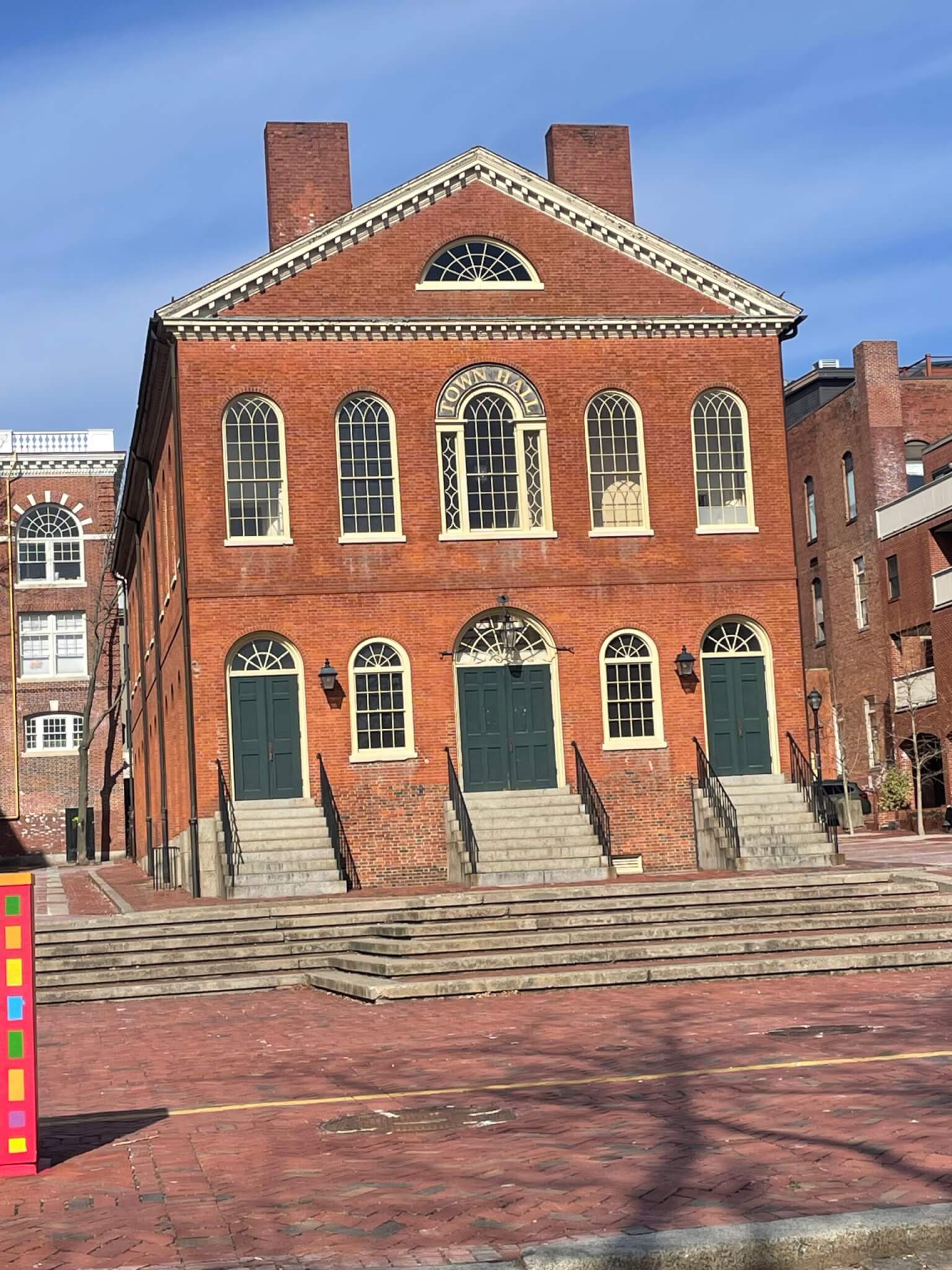 A three story brick building in a federal style with large arched windows and doors facing a paved courtyard.