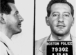 A profile and face on shot of a man with a five o'clock shadow. He has a Boston police prisoner placard around his neck.