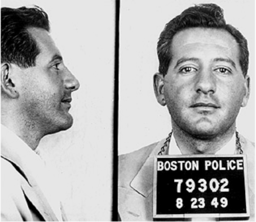 A profile and face on shot of a man with a five o'clock shadow. He has a Boston police prisoner placard around his neck.