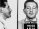 A profile and face on shot of a man with a five o'clock shadow. He has a Boston police prisoner placard around his neck.