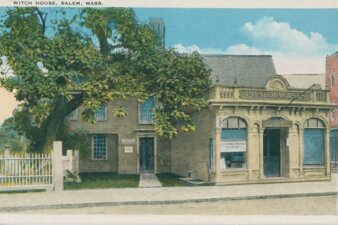 A postcard of a colonial house with a more modern storefront closer to the street. There is a large tree covering most of the hosue