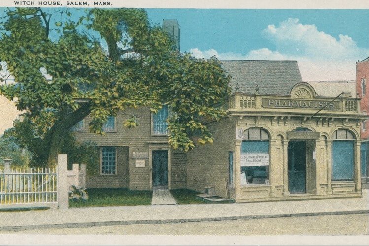 A postcard of a colonial house with a more modern storefront closer to the street. There is a large tree covering most of the hosue