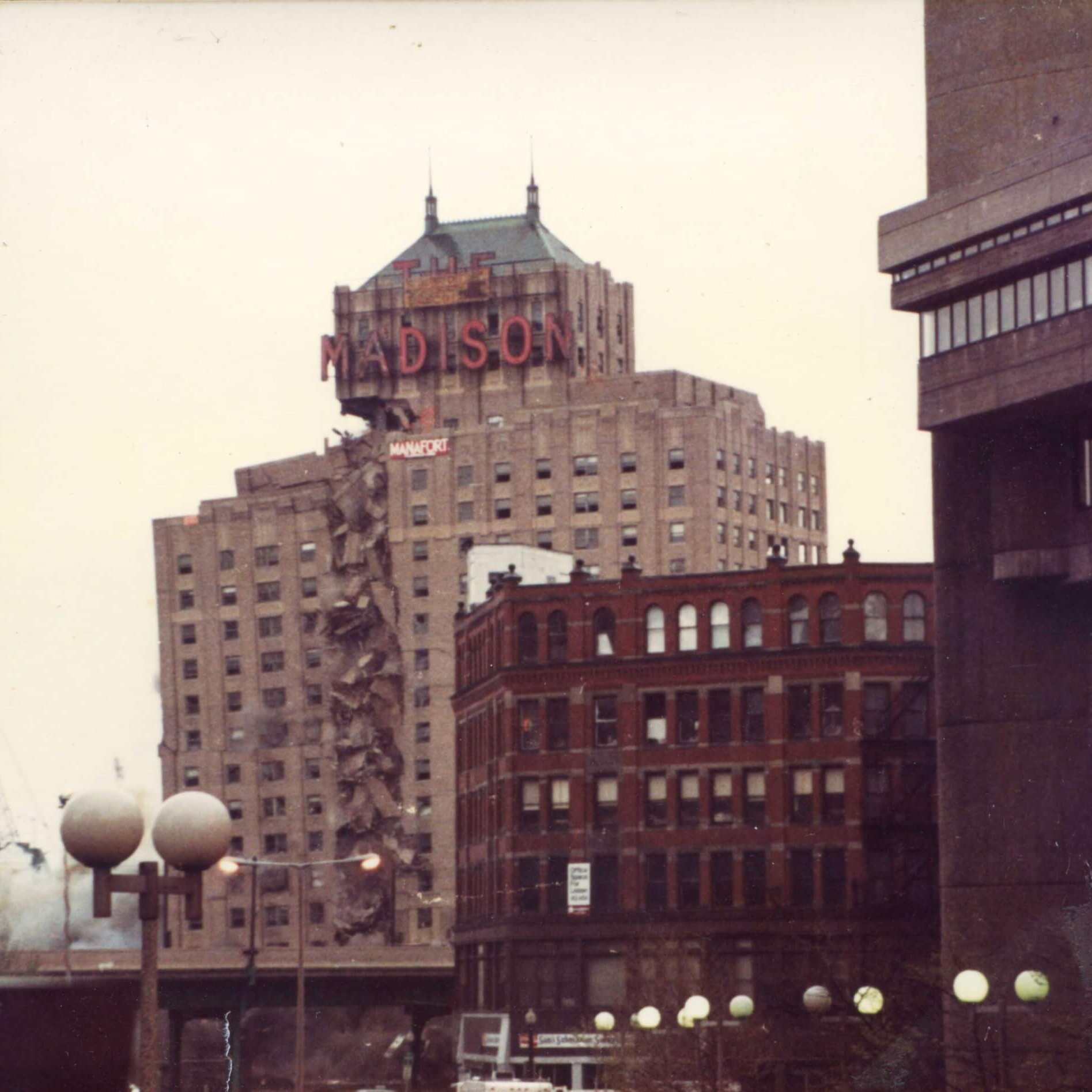 A tall hotel with the marquee that says Madison. The left side is collapsing and the dust cloud is bigger.