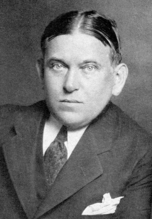 A portrait of a man with a center part and slicked down hair in a suit.