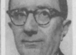 A man with glasses in a suit looking at the camera with a slight smile.