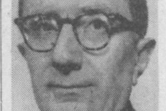 A man with glasses in a suit looking at the camera with a slight smile.