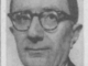 A man with glasses in a suit looking at the camera with a slight smile.