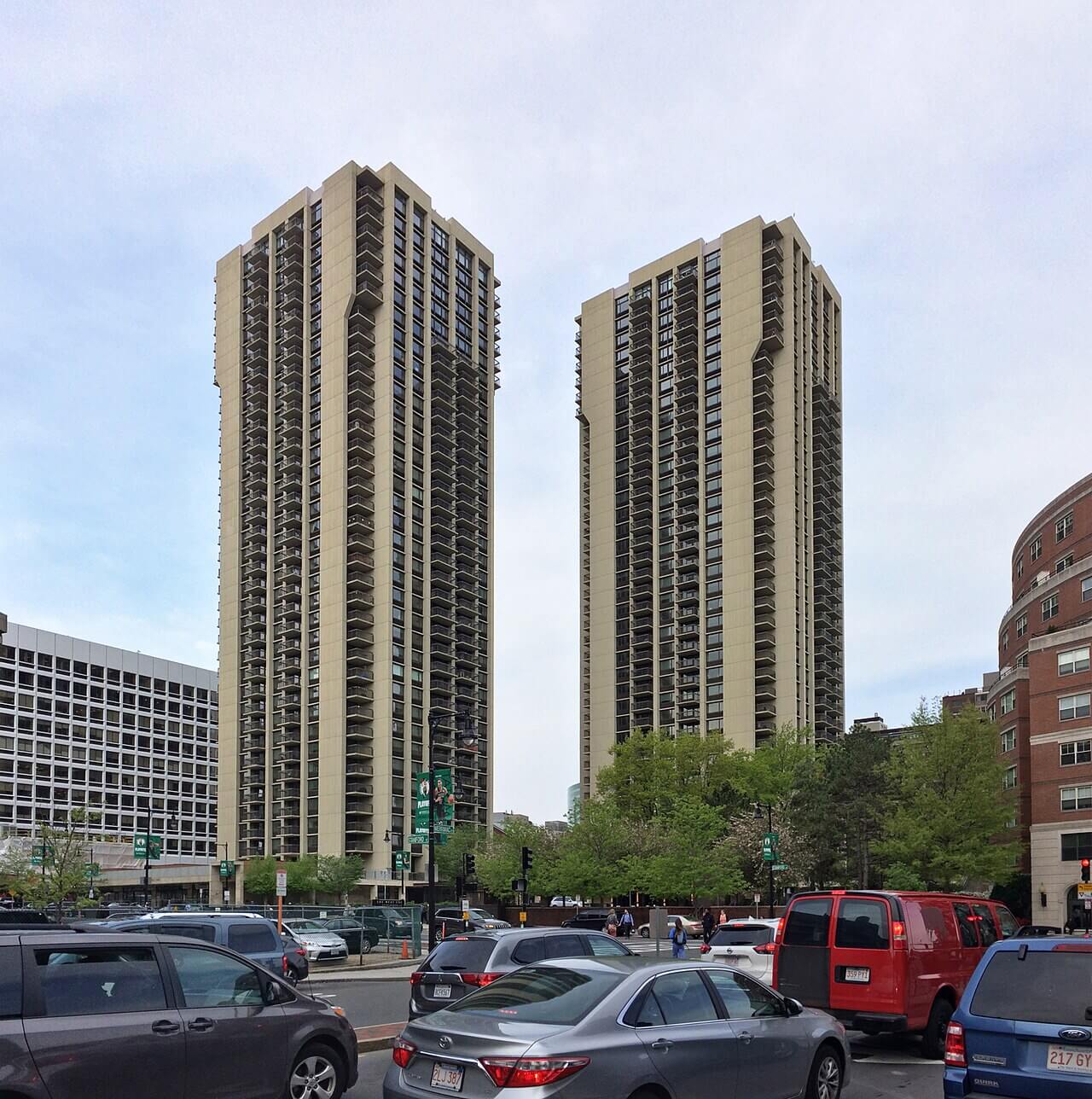 Two large residential towers with high balconies behind a traffic filled street.