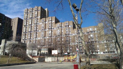 A brutalist style building with several layered sections so it looks like stairs. There is a playground in the foreground.
