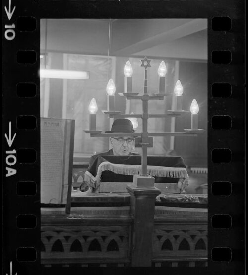 A man in a black hat standing behind a candelabra with a star of David on top of it.