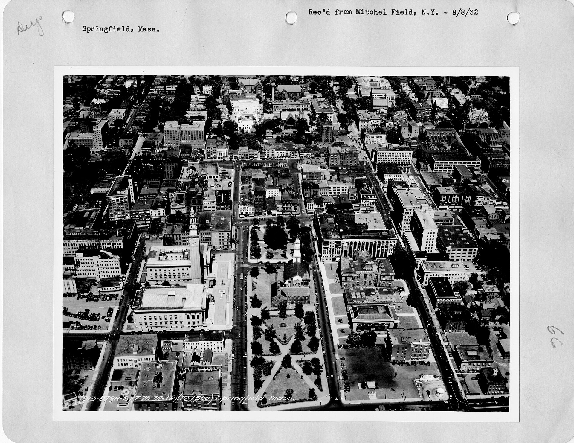Black and white aerial image of a mid size city over a central commons and several churches.