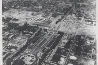 An aerial view of a neighborhood with a large train terminal at the bottom left. There is a gash through the area as buildings have been torn down for a highway construction.