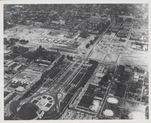 An aerial view of a neighborhood with a large train terminal at the bottom left. There is a gash through the area as buildings have been torn down for a highway construction.