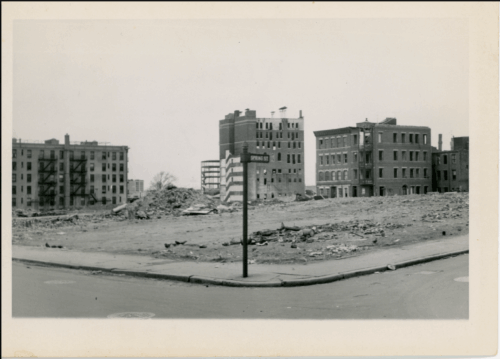 A street corner where the blocks behind it have been torn down leaving rubble behind.