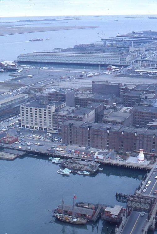 An aerial image of many short warehouses next to water. There is a channel with a small boat in the bottom third of the image.