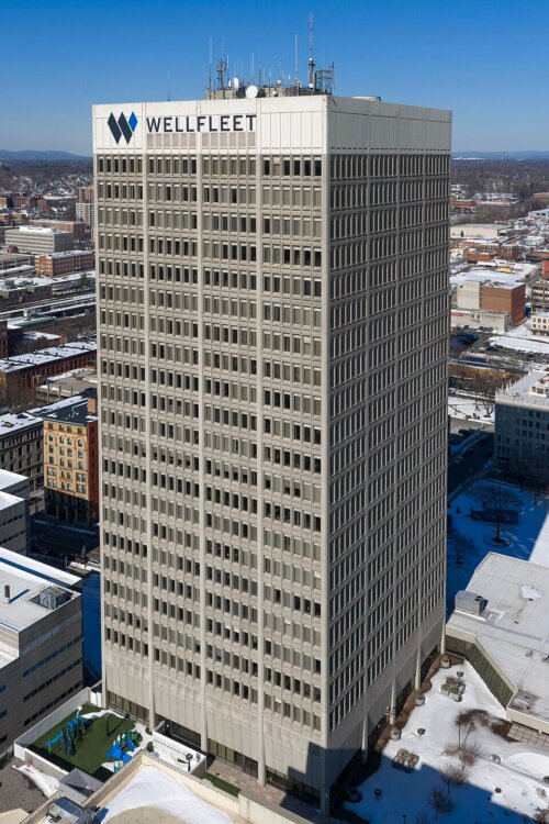 A tall office tower in the middle of a downtown area. There is snow on the flat roofs around the tower.