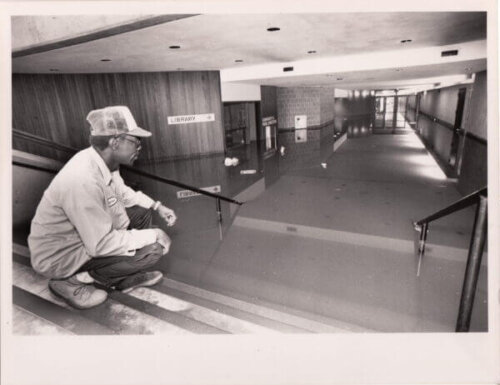 A man in work clothes looks down a flooded hallway.