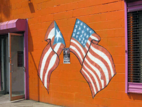 An orange wall with two painted flags crossed over each other. They are the Puerto Rican and American flag.