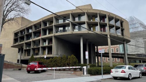 A concrete building with a curved facade. The curved portion is supported by exterior stilts.