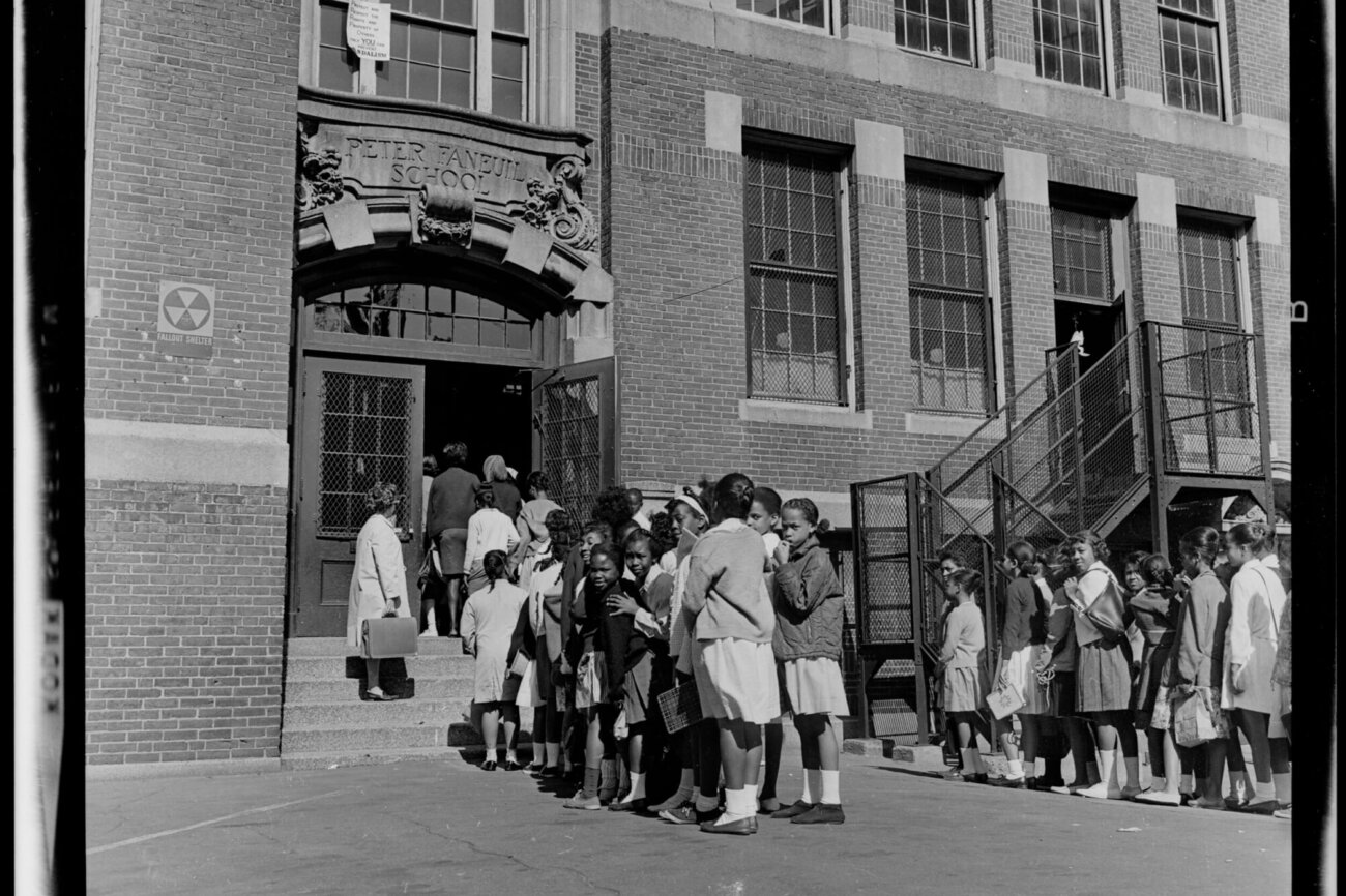 A group of elementary students wait to enter a school building.