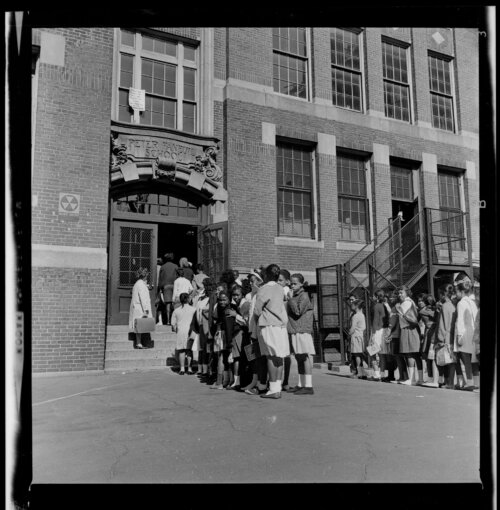 A group of elementary students wait to enter a school building.