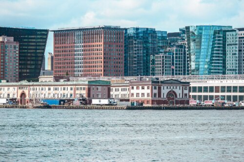 Low fish wharfs in the foreground with tall glass and steel high rises behind them. There is water in the foreground.
